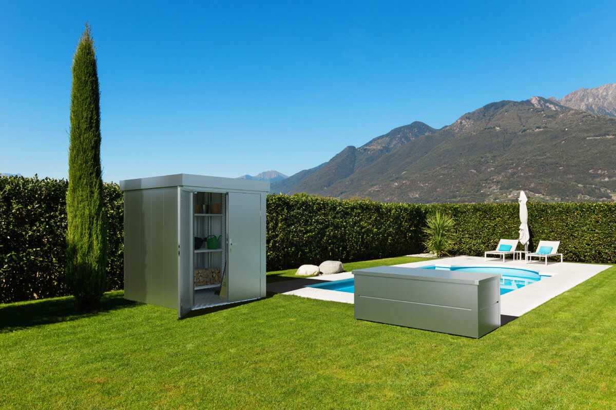 Ilesto Gartenhaus geöffnet und Gartenbox in silber metallic im Garten vor einem Pool aufgestellt.