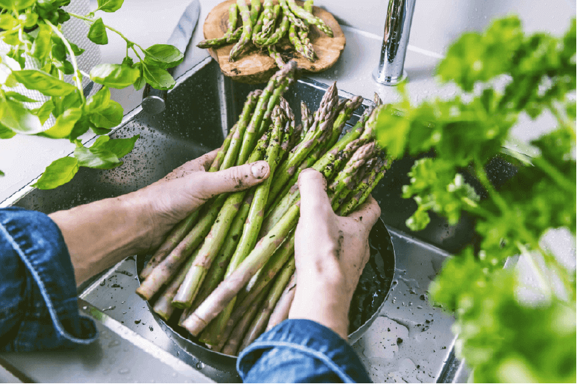 Mann wäscht grünen Spargel in Spüle