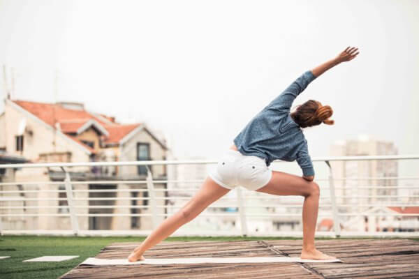 Frau macht Yoga am Balkon mit Yogamatte