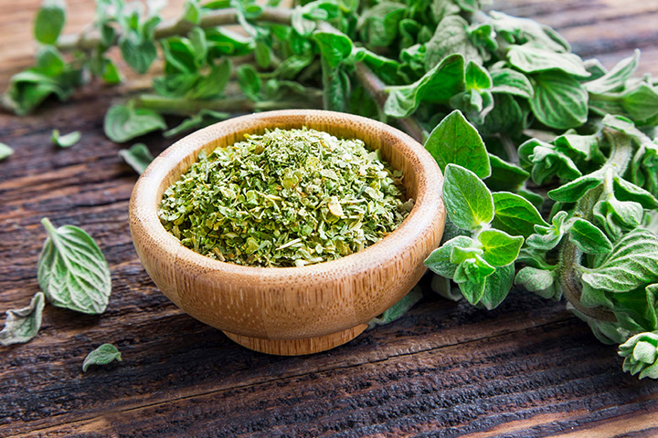 Eine Holzschüssel mit getrocknetem Oregano steht auf einem Holztisch, auf dem eine frische Oregano-Pflanze liegt