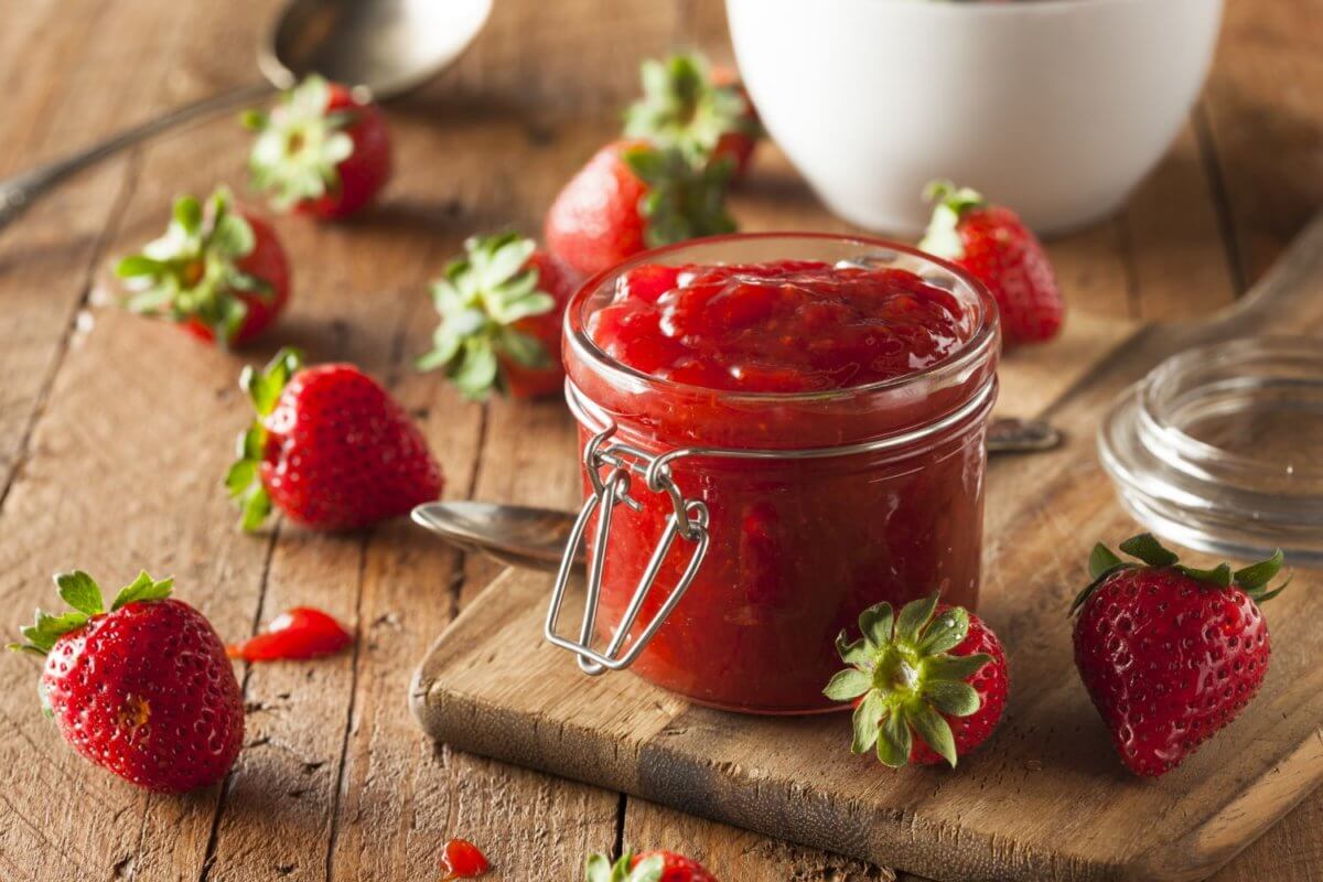 Erdbeermarmelade im Glas auf Holztisch, rundherum rote Erdbeeren