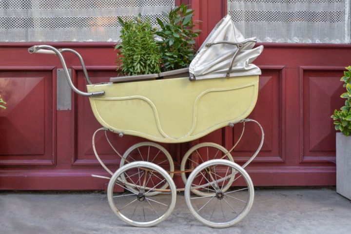 Man erkennt einen gelben Kinderwagen mit einer Pflanze drinnen.