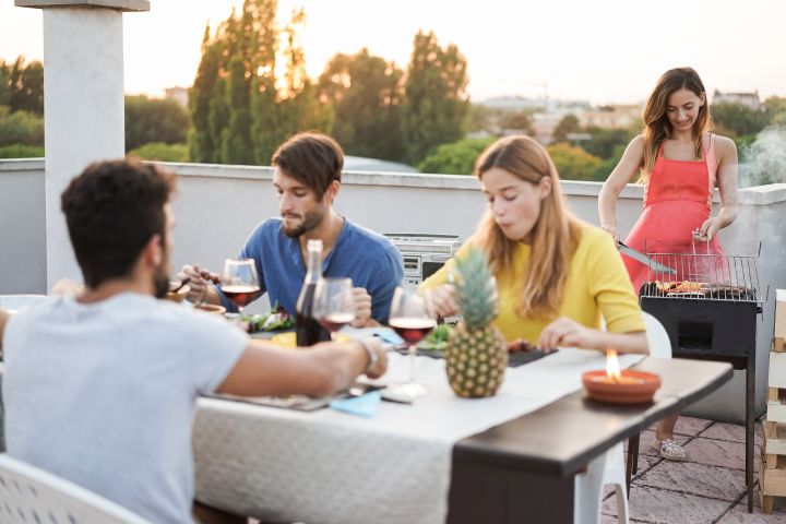 Freunde grillen auf einem Balkon und unterhalten sich.