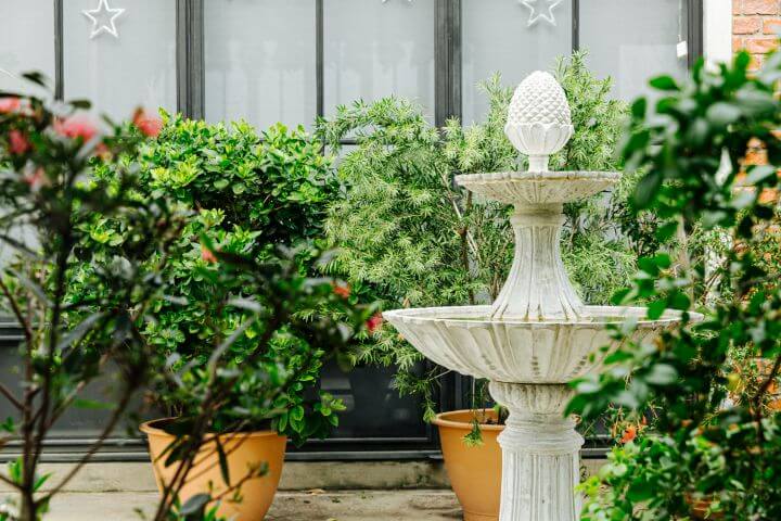 Weißer Springbrunnen in Mitten von grünen Pflanzen