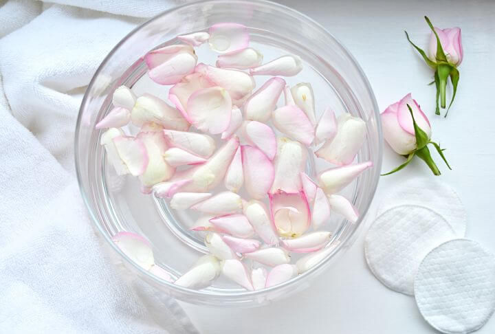 Wasserschale mit rosa Rosenblätter, daneben Wattepads und 2 rosa Rosen