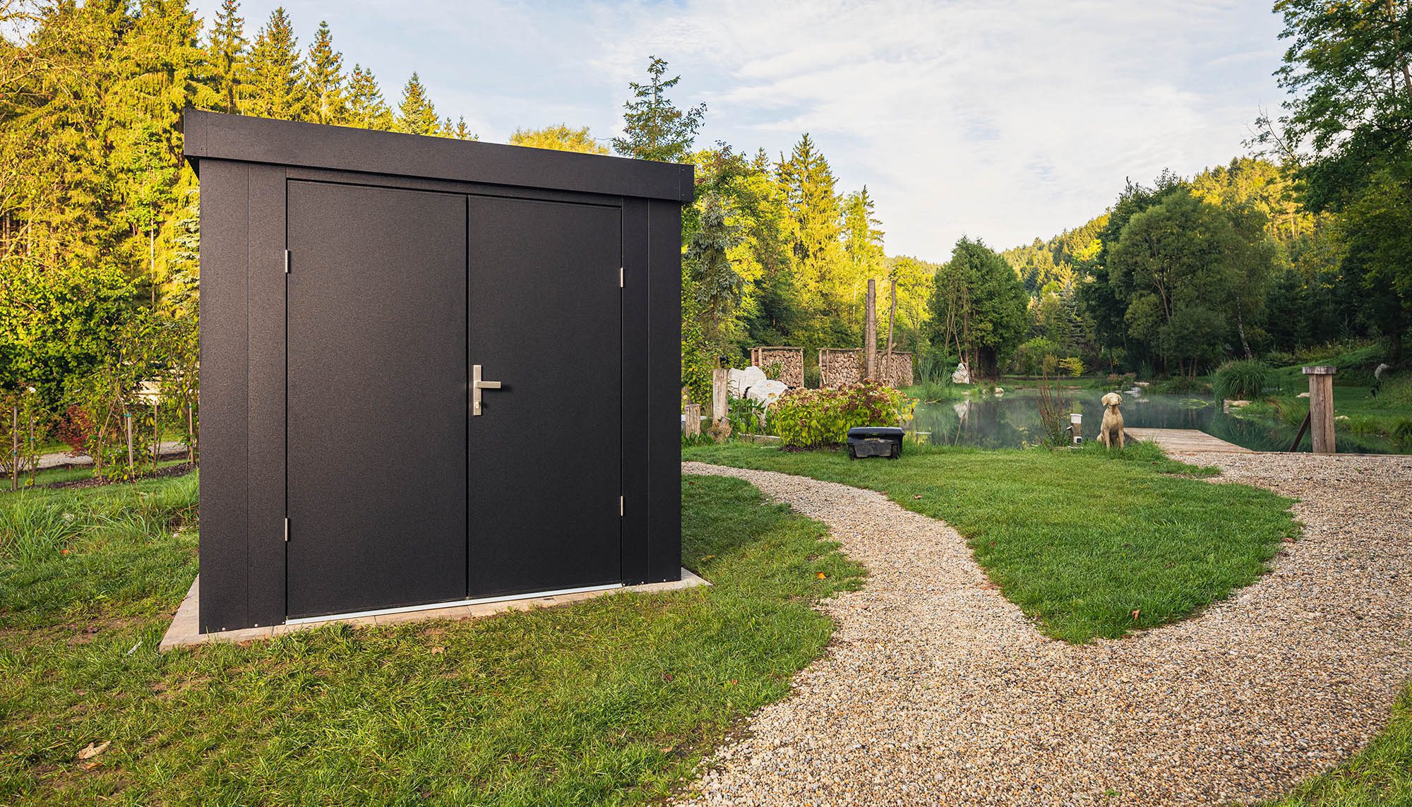 Ilesto Gartenhaus aus Stahl in anthrazit auf eiem großen Grundstück neben einem Gehweg