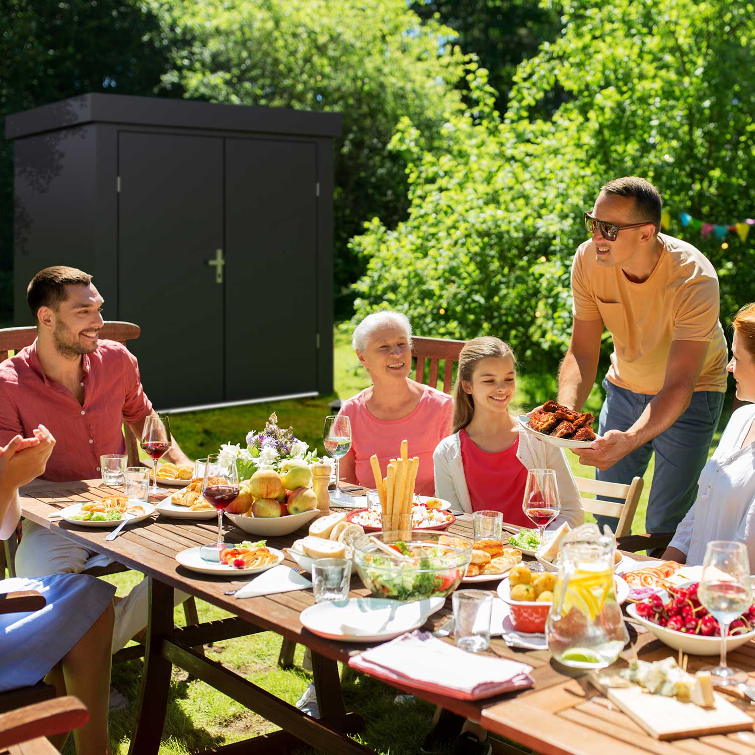 family having lunch in the garden / grey garden shed in the background