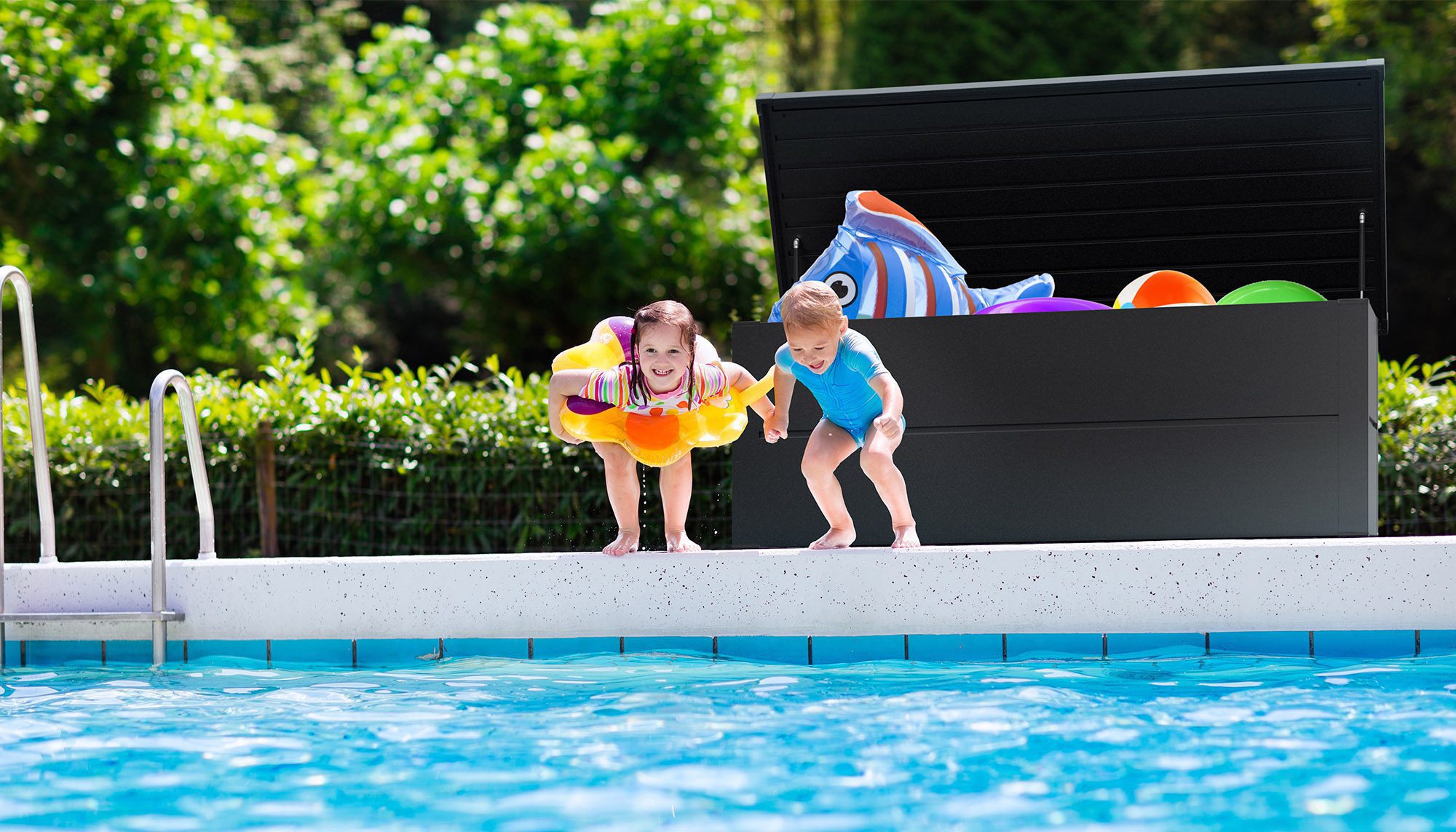 Ilesto Auflagenbox in anthrazit steht am Rande eines Pools gefüllt mit Spielsachen für Kinder und davor zwei Kinder, die gerade in den Pool springen