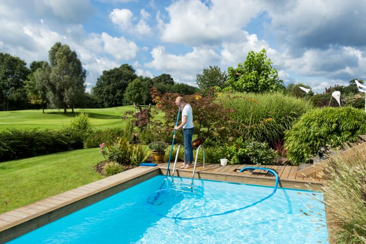 Mann reinigt einen Swimming Pool mit einem Teleskop