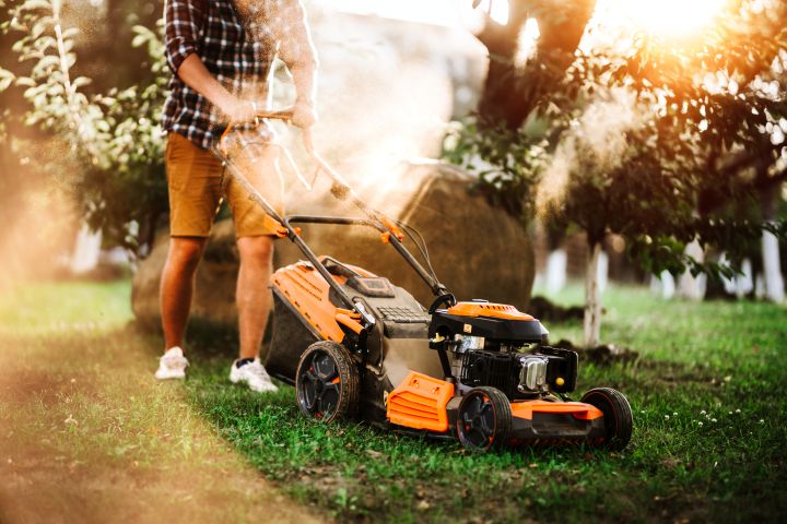 Mann in kurzer Hose mäht mit einem elektrischen Rasenmäher den Garten