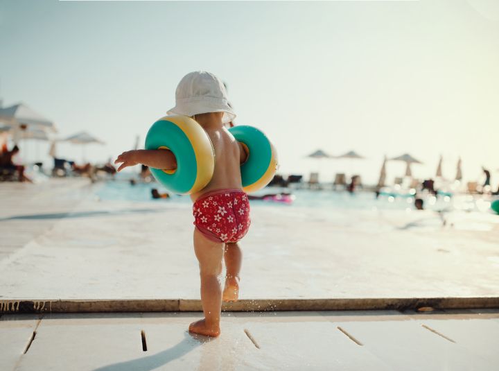 Baderegeln: kleines Kind mit schwimmflügel am Poolrand