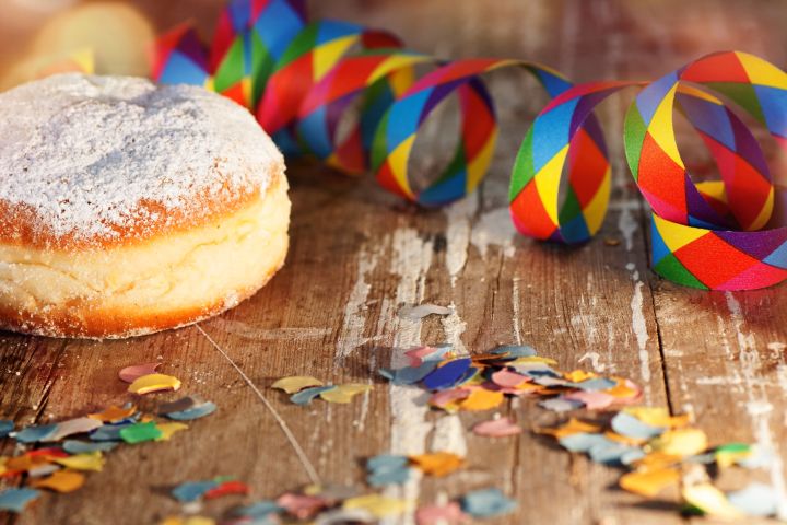 Man sieht einen Krapfen am Tisch liegen und eine bunte Luftschlange sowie Konfetti daneben liegen