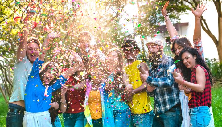 Man sieht ein paar Freunde, die fröhlich bunte Konfetti durch die Luft schmeißen und dabei eng zusammenstehen und lachen