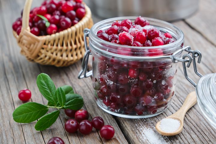 Gezuckerte Kirschen in durchsichtigem Glas, Holzlöffel, geflochtener Korb mit Kirschen im Hintergrund