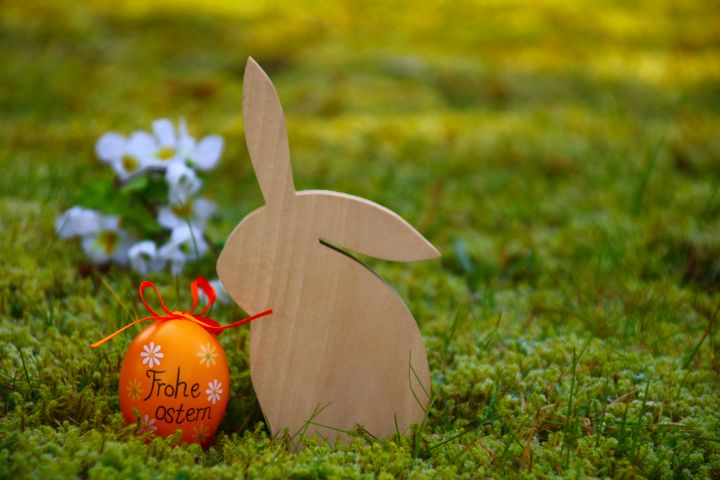 Eine Holzfigur in Form eines Hasen und daneben ein organgenes Osterei in der Wiese 